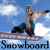 A snowboarder in a beige jacket and teal pants performs an aerial trick against a blue sky with white clouds, with the word "Snowboard" displayed below.