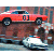 A red classic car with black wheels and a white roof is positioned above a brown vehicle, both on a reflective surface under a blue-toned background.