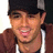 Pixelated close-up of a person wearing a dark cap and brown jacket over a white shirt, with a blurred background.
