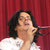 Pixelated image of a person with dark hair wearing a white top against a red striped background.
