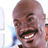 Pixelated static image of a smiling person with dark skin tone, visible facial features including eyes, nose, mouth, and mustache, set against light background with blue and orange elements on sides.