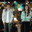 Two people in light blue and white clothing stand close together, one person's head moves toward the other as if to kiss.