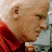 Static 48x48 pixel icon showing a close-up profile of an older man with light skin, short white hair, and a red collared shirt against a blurred background.