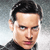 Pixelated close-up of a person with dark hair, light skin, and blue eyes wearing a dark high-collared shirt against a gradient background.