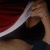 A person in a dark blue shirt with red and white stripes on the sleeve, holding a white object near their face, with a white background in the bottom-right quadrant.