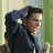 A pixelated image of a person with dark hair in a dark jacket, set against a green and beige background, with overlaid text on a blue field.