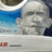 Pixelated static image of a stylized human face with closed eyes, blue and white background elements, and small red-and-gray shapes at the bottom.
