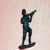 Pixelated teal figure in dynamic pose holding a long object, standing on a dark base against light background.