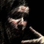 Pixelated static image of a person with dark hair holding a long object against a black background.