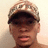 Pixelated close-up of a person wearing dark sunglasses and a light-colored cap with indistinct text, against a pale background.