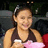Pixelated image of a person with dark hair tied back, wearing a sleeveless top and holding pink fabric against a blurred background.