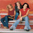 Three figures in casual clothing stand against a gradient background with warm tones, one holding a large dark object.