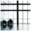 Silhouetted figures stand near a large grid-patterned window with reflective flooring, viewed from a low angle.
