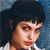 Pixelated close-up of a person with dark hair and light skin wearing a white shirt against a blue background.