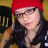 Pixelated image of a person wearing red headwear, dark clothing, and glasses with visible background elements.