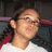 Pixelated close-up of a person with light skin tone wearing glasses and dark hair, set against a blurred background with red and white elements.