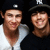 Two pixelated figures in dark hats with white accents stand side-by-side against a black background, one wearing light clothing and the other dark.