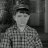 Grayscale pixelated image of a person wearing a cap and patterned shirt against a dark background.