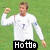 Pixelated image of a person in white long-sleeve shirt with dark number 7 on chest, standing against green background, right arm raised.