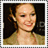 Pixelated portrait of a smiling woman with light brown hair in an updo, wearing a beige top against dark background.