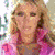 A woman with long blonde hair appears in multiple poses: standing, singing into a microphone, and smiling closely. She wears pink clothing and dark shorts or a skirt.