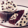 A chocolate cupcake with white frosting and chocolate chips, a slice of chocolate cake, and a chocolate chip cookie on a plate.