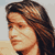 Pixelated close-up of a person with long brown hair, light skin, and a neutral expression against a light background.