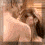 A woman with long dark hair lies on a textured surface, her head resting on a light-colored pillow, wearing a light-colored top with a low neckline.