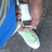 A person's hand holds a white smartphone with green accents against a dark textured background, partially covered by blue fabric.