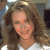 Pixelated close-up of a person with light brown curly hair wearing a white top, set against a blurred background with indistinct shapes and muted colors.