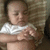 A baby in a white shirt lies on a striped surface, with hands positioned differently