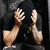 Two pixelated hands with light skin tones raised against a dark background, one hand showing fingers and the other a clenched fist.