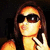 Pixelated static image of a person with long brown hair wearing dark sunglasses, holding a phone to their ear against a dark background.