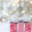 Pixelated static image showing three pink gift boxes with dark red ribbons against a light blue and white background with scattered beige shapes.
