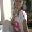 A pixelated image shows a person in a white sleeveless top with red accents, standing indoors near a window and dark furniture.