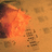 Pixelated image with orange background, left side shows blurred object resembling a flower or fabric on textured surface.