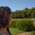 A pixelated outdoor scene showing a person's back with dark hair, green grass, trees, and blue sky.