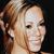 Pixelated close-up of a person with light brown hair tied in a high ponytail, smiling with visible teeth against a dark background.
