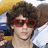 Pixelated image of a person with curly brown hair wearing red sunglasses, next to yellow background with red text.