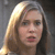Pixelated close-up of a person with light brown hair, neutral expression, and visible mouth, set against a dark gray background.