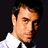 Static pixelated image of a person's face and upper torso in formal attire against dark background, rendered at low resolution with visible dithering and color banding.