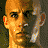 Pixelated image of a bald man with serious expression, showing three sequential head positions against dark background with text "Riddick" and "THE CHRONICLES OF RIDDICK".