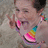 A pixelated image shows a person with dark hair making a peace sign with their right hand, wearing a colorful rainbow-patterned hat with pink, orange, yellow, green, and blue sections.