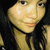 Pixelated close-up of a person with long dark hair, light skin tone, and neutral expression against dark background.