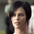A pixelated close-up of a person with dark hair, light skin, and a neutral expression, set against a blurred background with muted tones.
