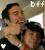 Two people embrace in a close-up; one wears a black hat and red necklace, the other has dark hair. A white heart appears on the left side of the first frame.