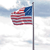 Static pixelated image of a flag on a pole with red and white stripes and a blue field with white stars against a light blue sky background.