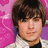 A pixelated image of a person with brown hair and light skin wearing a white jacket over dark clothing against a pink patterned background.