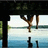 Pixelated static image shows a figure in mid-air with arms outstretched against layered background of dark structure, light sky, and blue water.