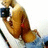A person in a red bikini top and blue shorts holds a black camera, positioned in a seated pose with legs extended.